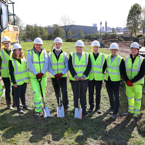 A group of people in hard hats and high jackets, holding spades