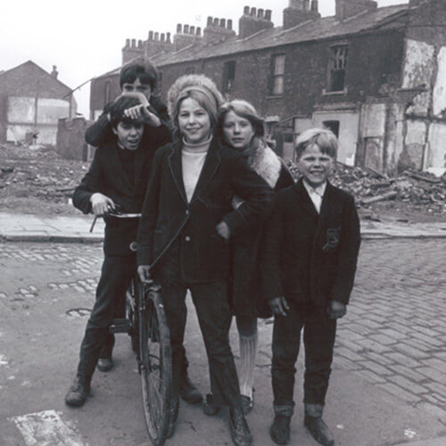 A historical black and white photo of five young people, on a cobbled street