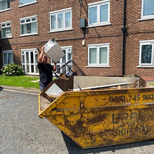 A man putting a box into a skip