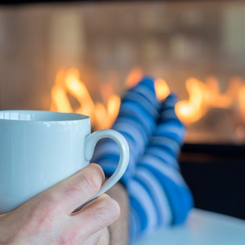 A person wearing socks, holding a mug, in front of a fireplace