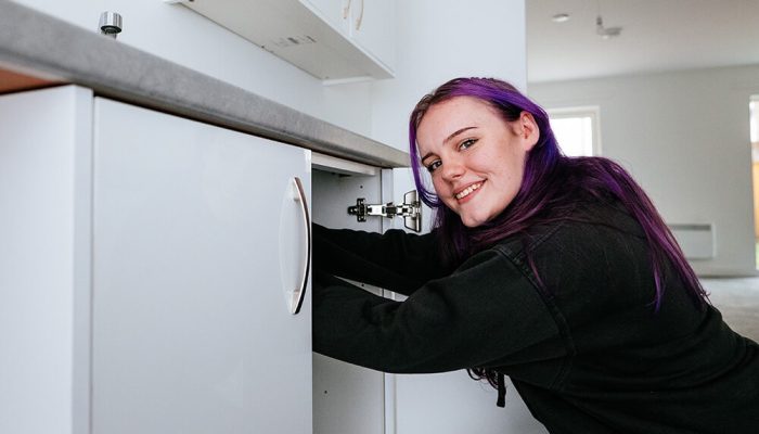 A young woman smiling, working on fitting a kitchen cabinet
