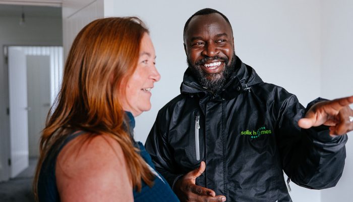 A smiling woman, stood alongside a man in Salix Homes uniform, pointing across the room