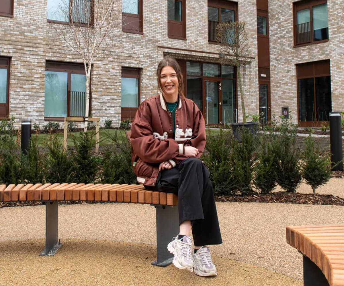 A young woman sat on a bench outside a brand new apartment building