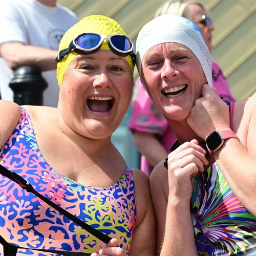 Two smiling women, wearing swimming costumes and swimming caps